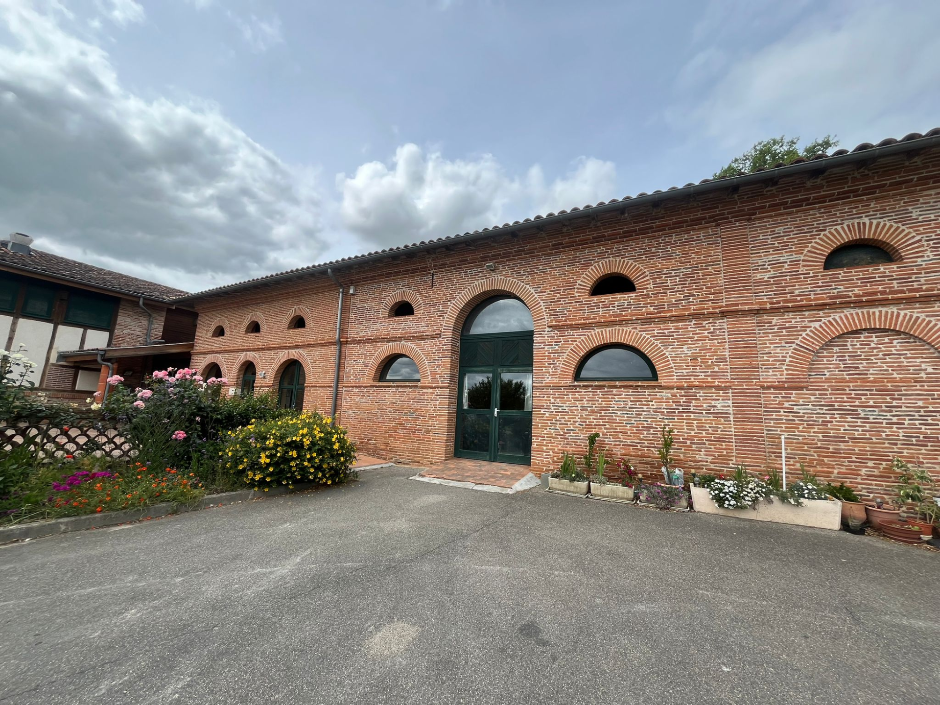 Bâtiment en brique avec arches, fleurs et parking.