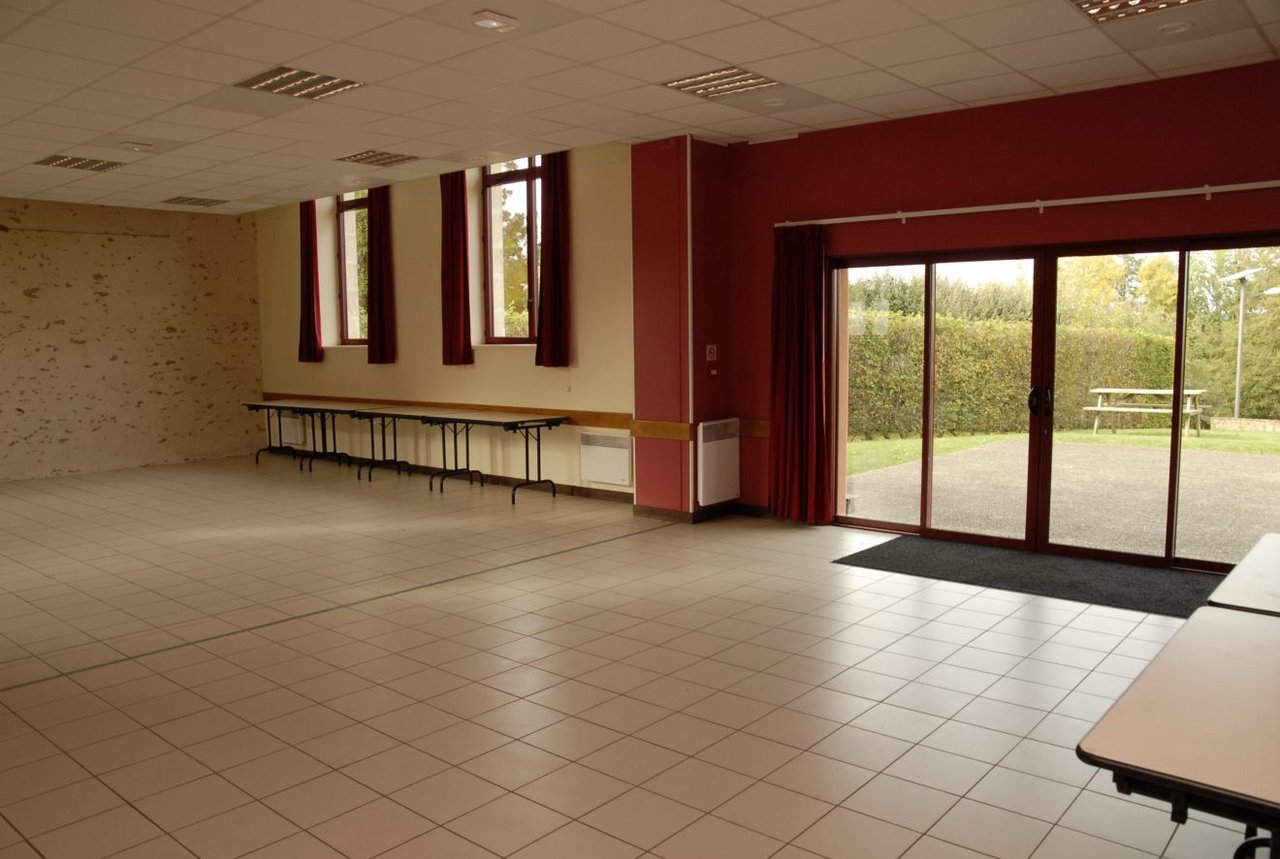 Salle avec tables, chaises, porte vitrée et fenêtres.