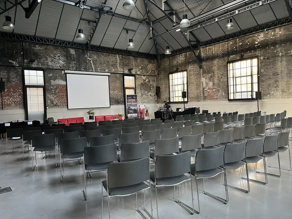 Salle avec chaises, tableaux, écran, vidéoprojecteur, et fenêtres.