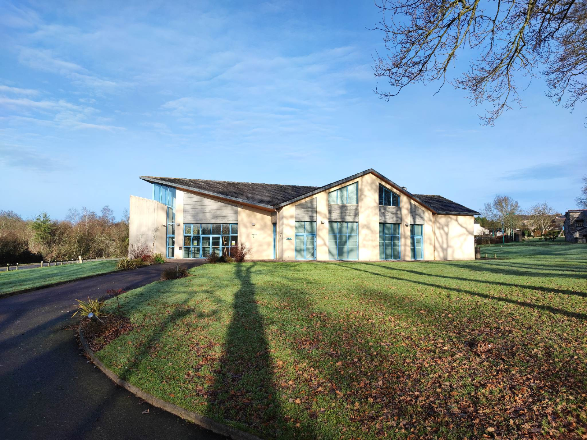 Bâtiment moderne avec grandes fenêtres, pelouse, arbre et ciel bleu.