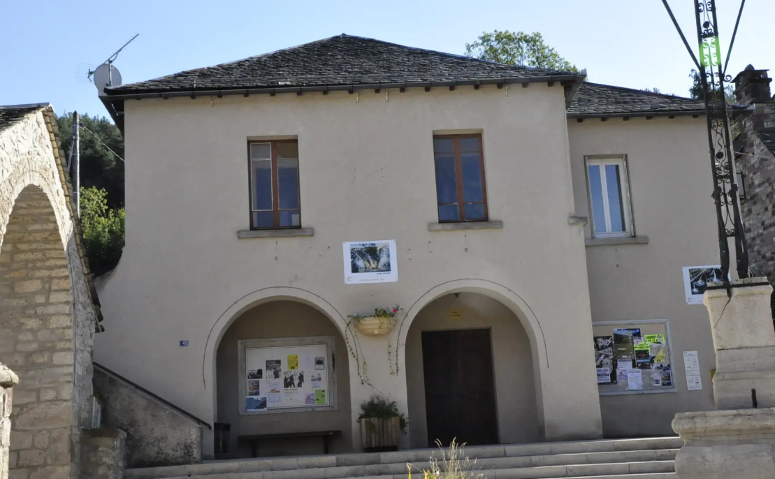 Bâtiment avec deux portes et deux fenêtres, affiches, plantes et antenne sur le toit.