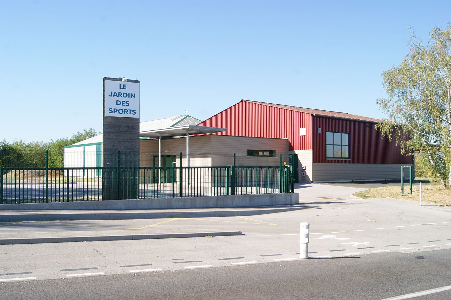 Bâtiment avec panneau "Le Jardin des Sports", clôture, route, et arbre.