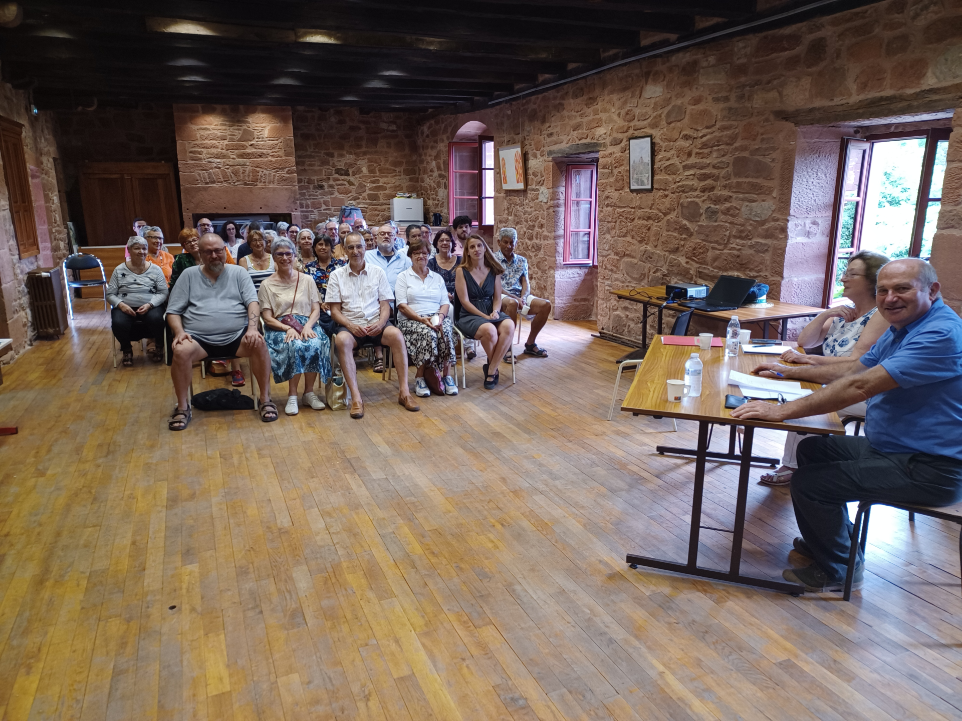 Salle avec parquet, murs en pierre, chaises, tables, projecteur et rideau.