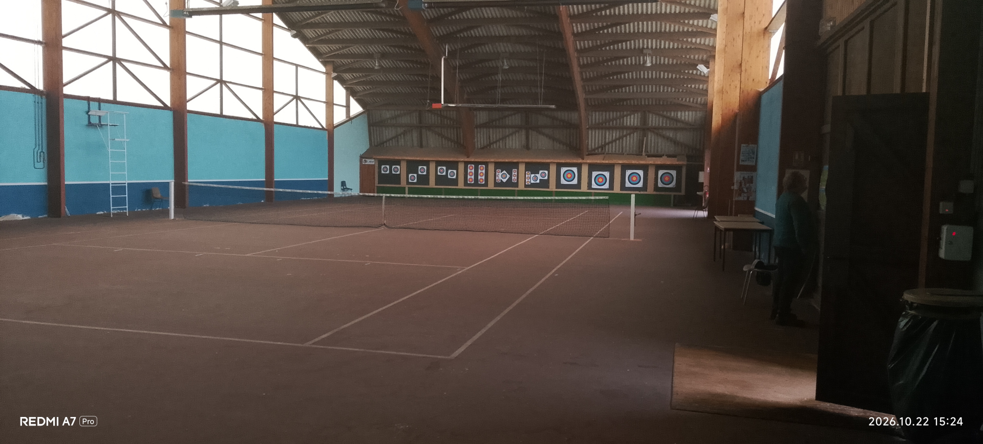 Salle intérieure avec terrain de tennis, cibles de tir à l'arc, table et chaises.