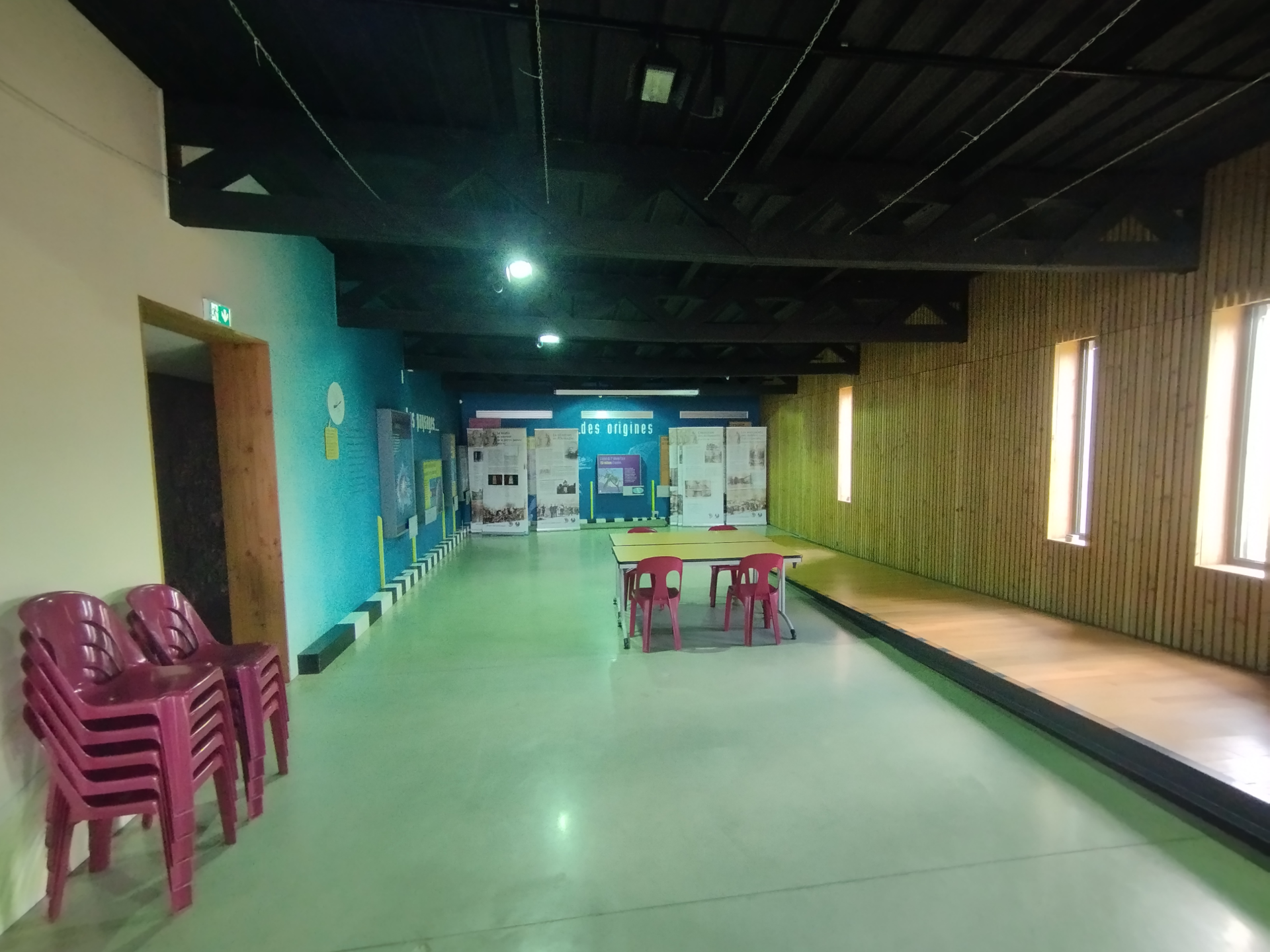 Salle spacieuse avec chaises, tables, murs colorés et fenêtres.