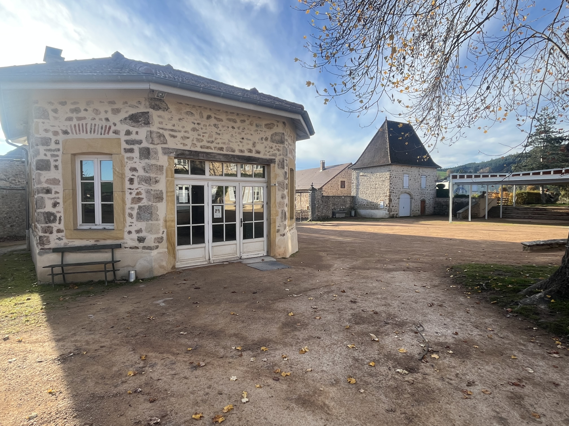 Bâtiment en pierre avec porte, fenêtre, banc et cour.
