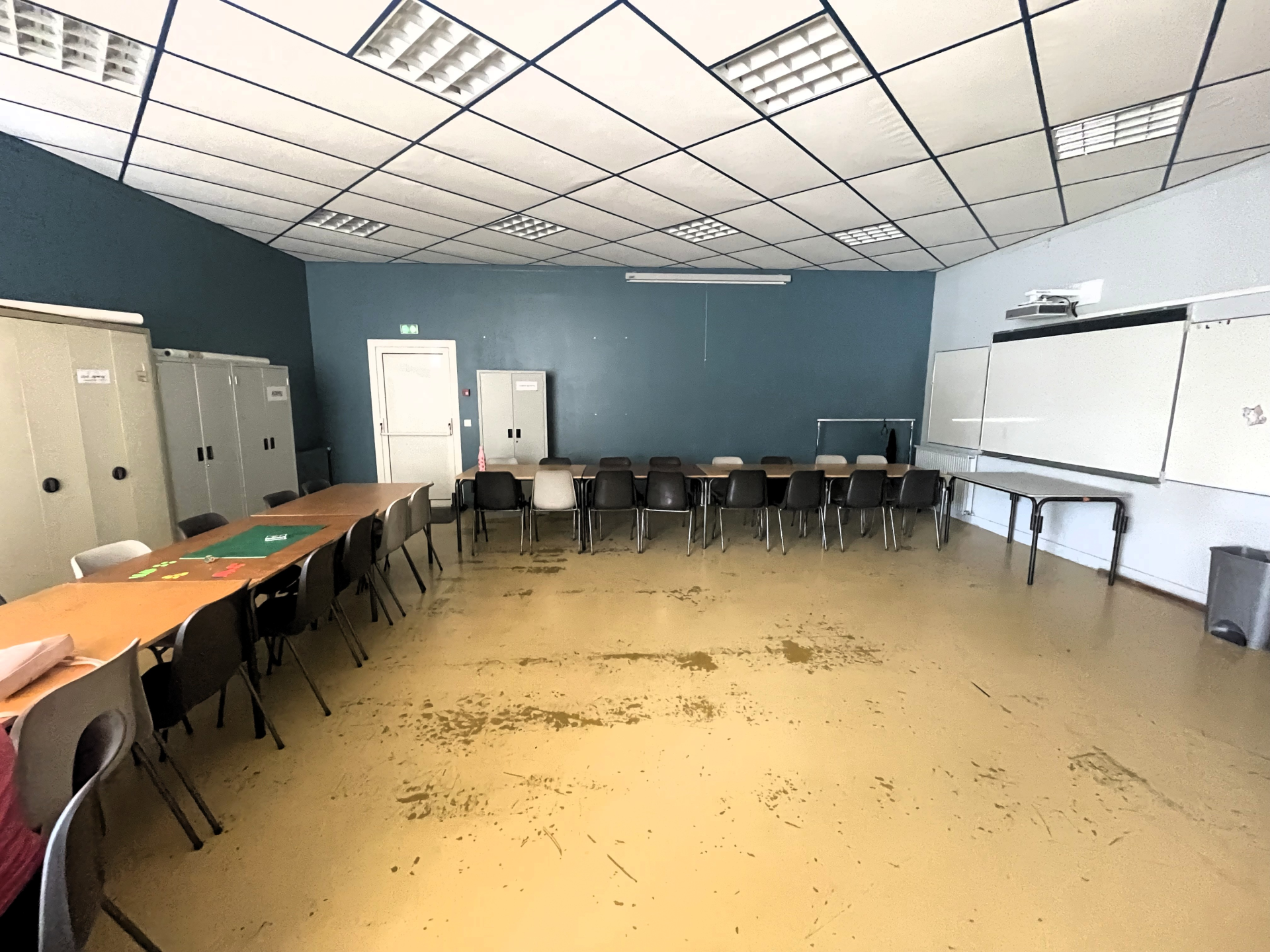 Salle avec tables, chaises, armoires, tableau blanc et projecteur.