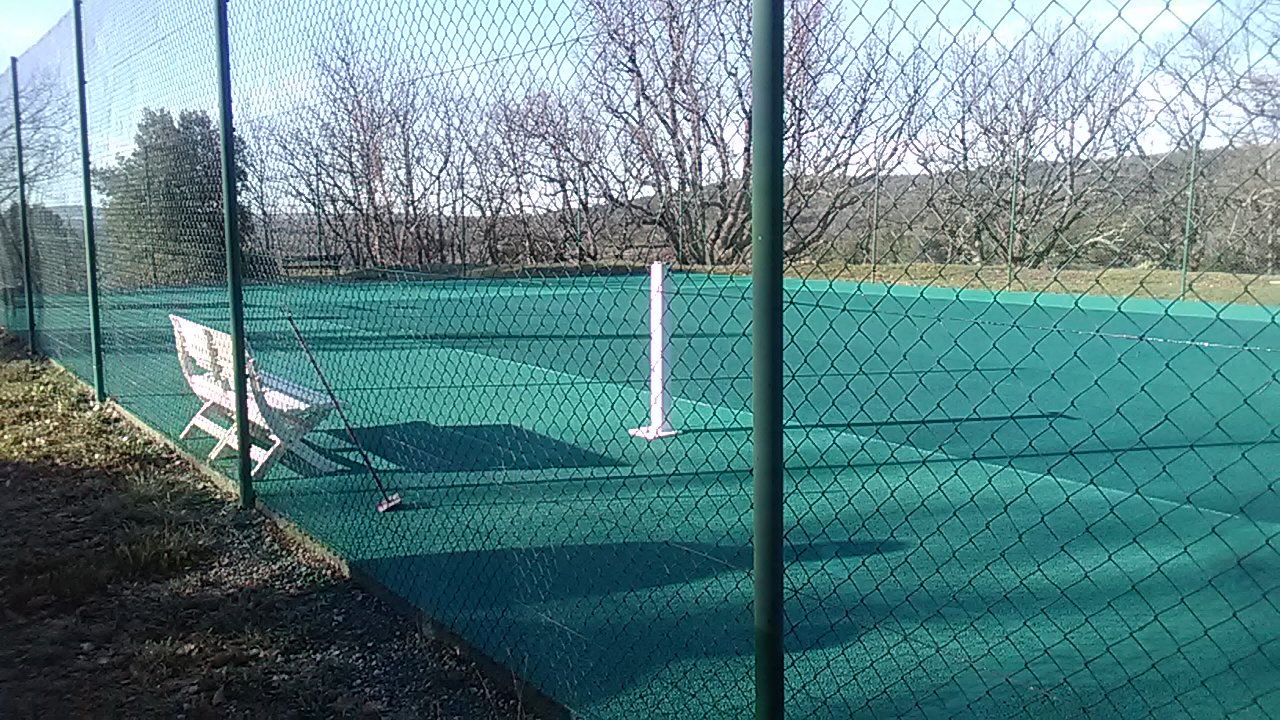 Terrain de tennis avec filet, chaises et clôture.