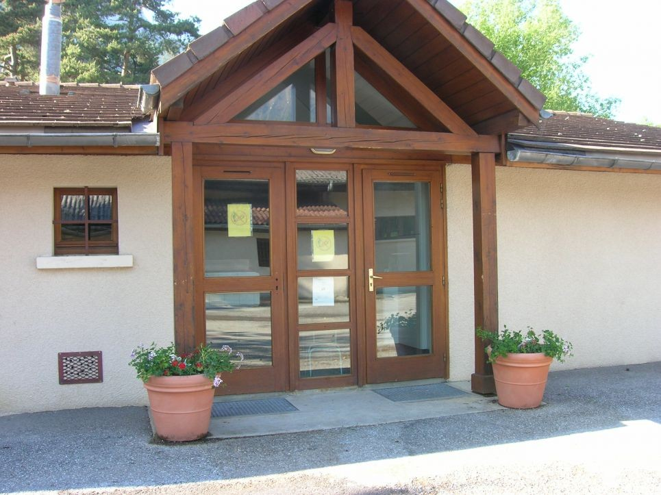 Entrée avec double porte en bois, fenêtres, pots de fleurs et auvent en bois.