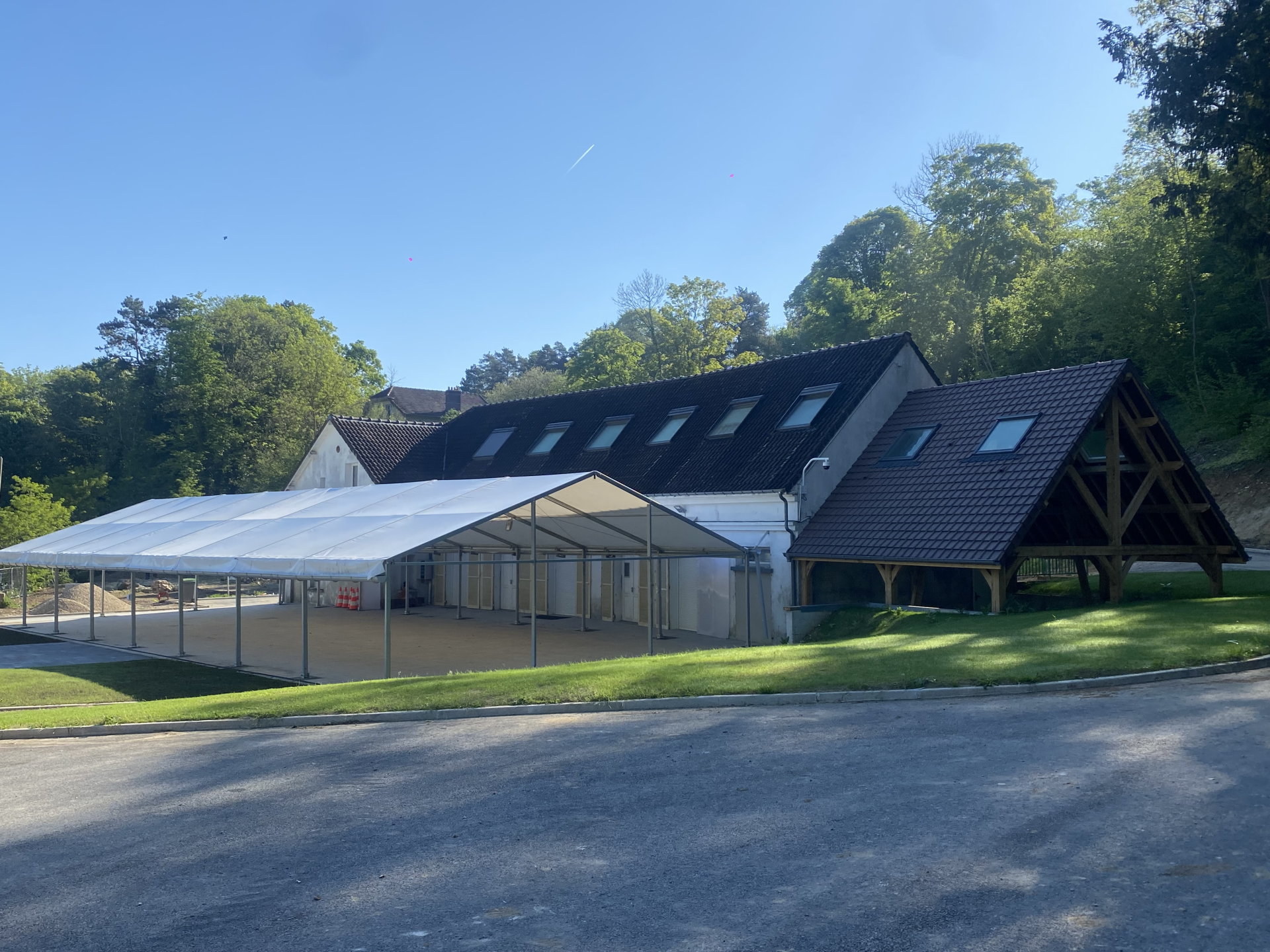Bâtiment avec structure en bois, toit incliné, abri extérieur et parking adjacent.