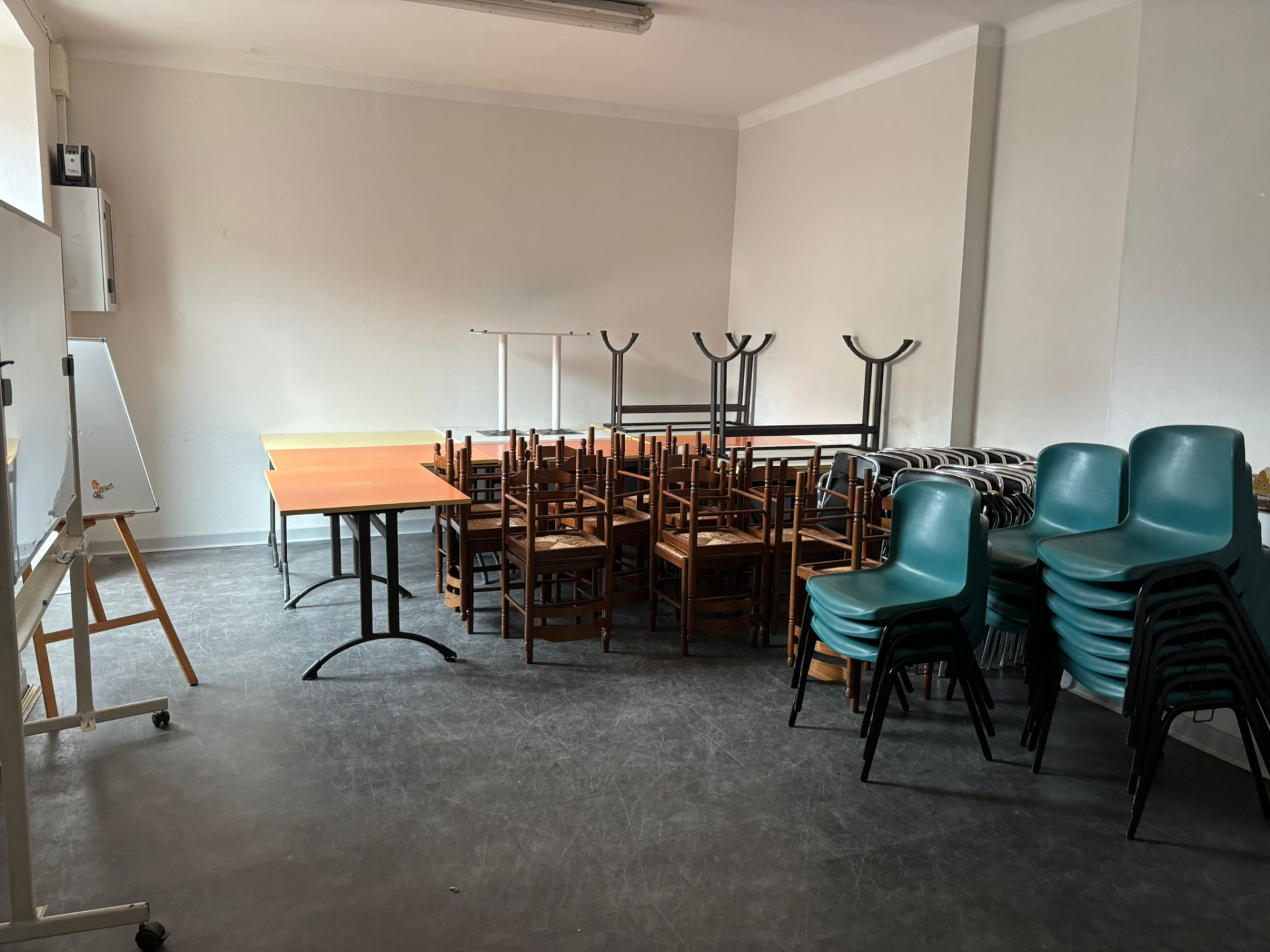Salle avec tables, chaises, chevalet et tableau blanc.