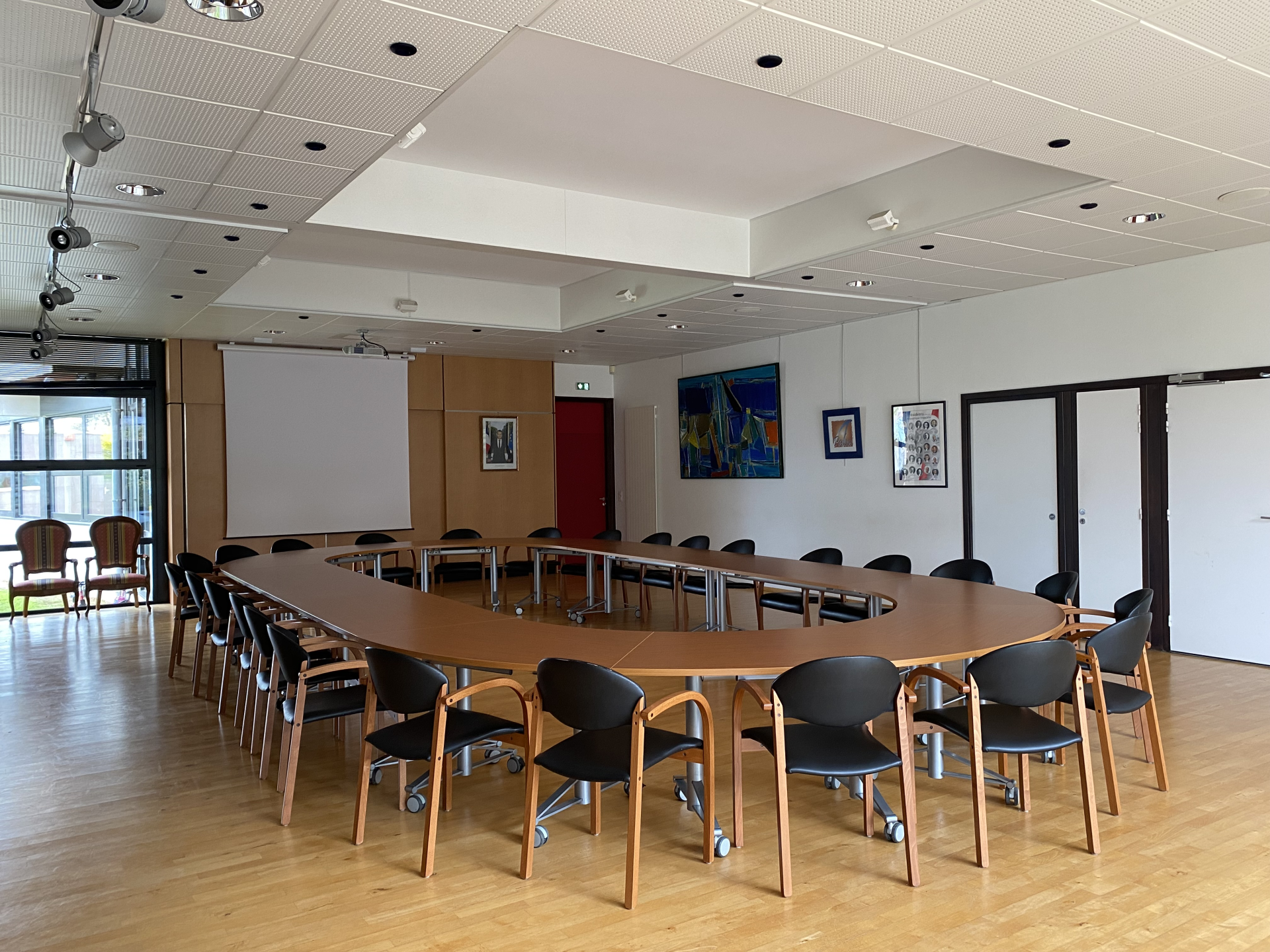 "Salle de réunion avec table ovale, nombreuses chaises, tableaux et porte."