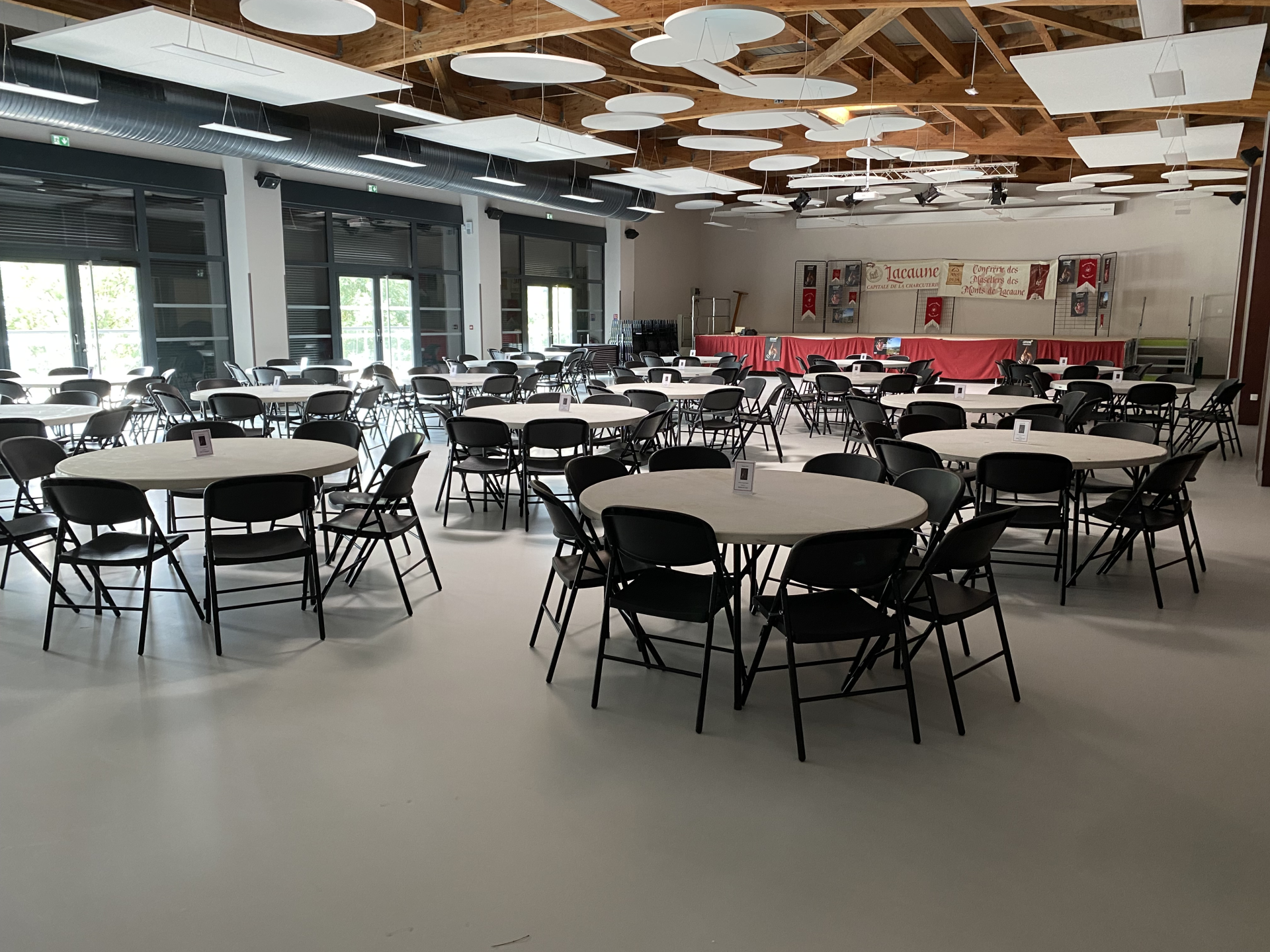Salle avec tables rondes, chaises, estrade et bannières.