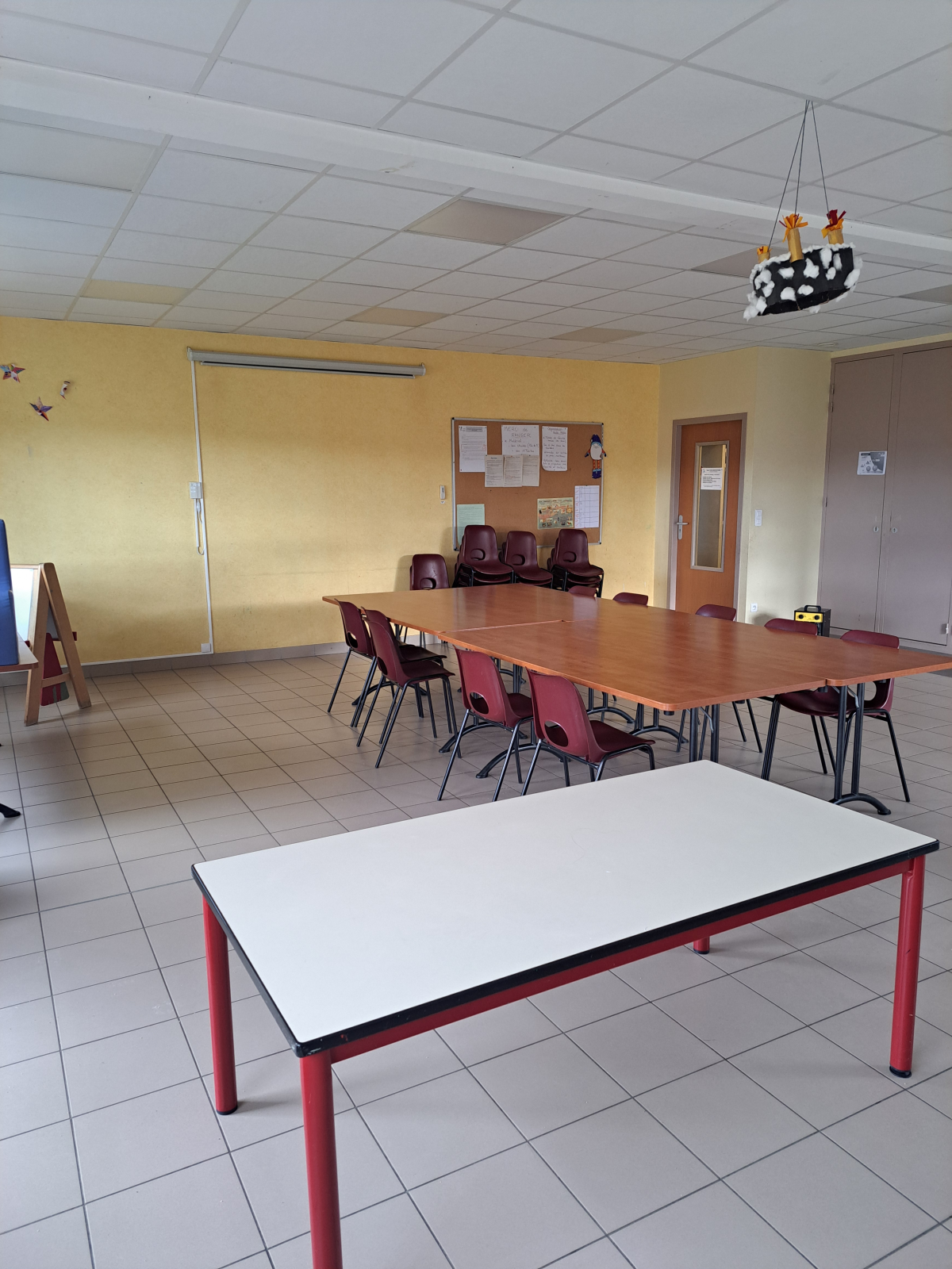 Salle avec tables, chaises, tableau blanc, porte-manteau et lustre.