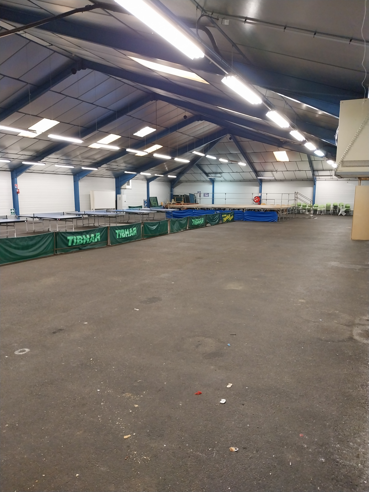 Salle spacieuse avec trampolines, sol en béton, murs blancs et plafond haut éclairé.