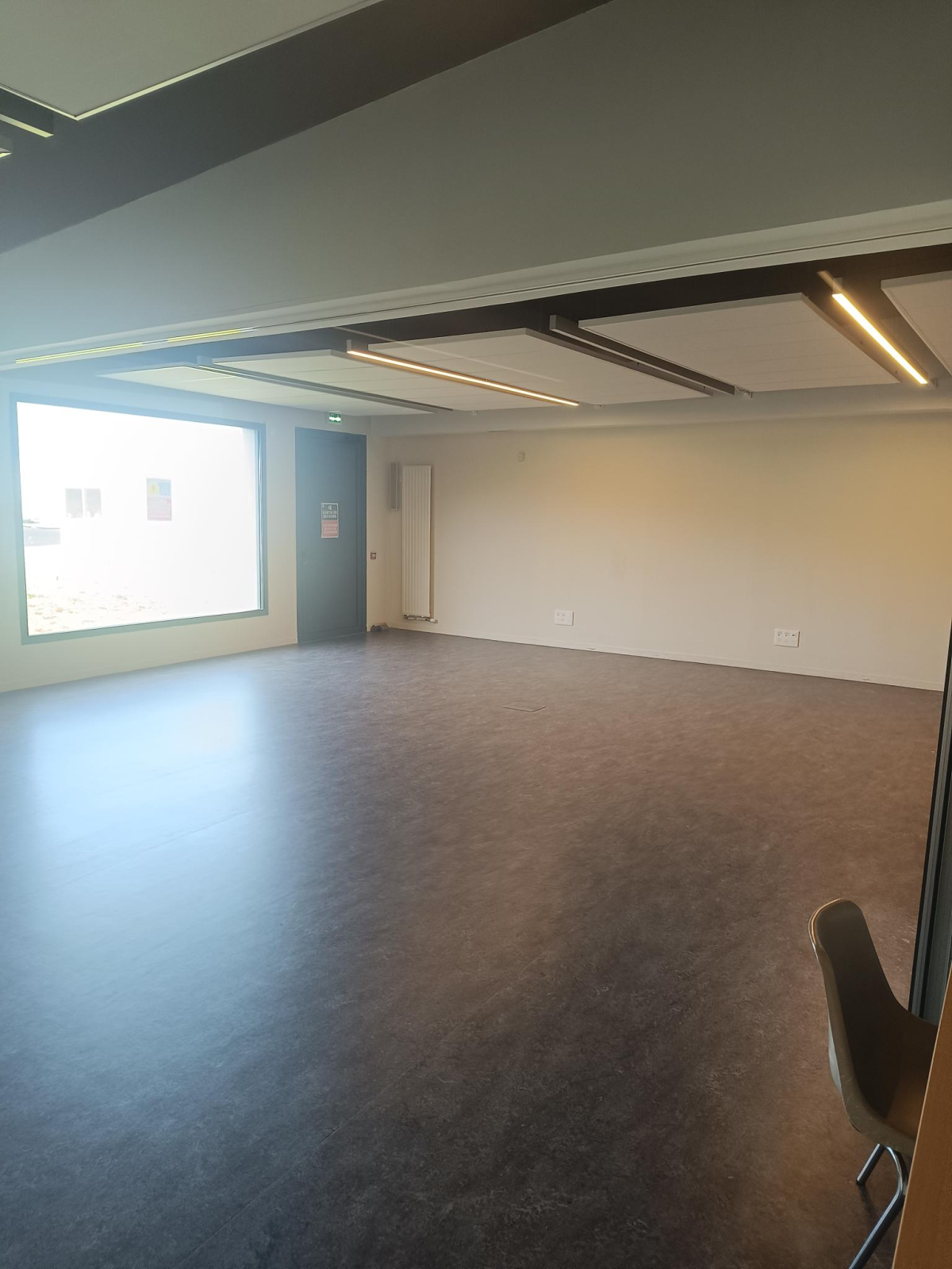 Salle vide avec sol, murs, fenêtres, portes et éclairage au plafond. Une chaise visible.