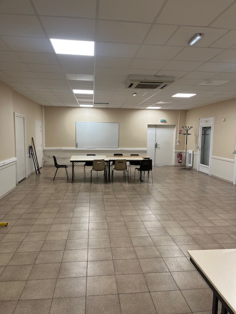 Salle vide avec table, chaises, tableau blanc, climatiseur, porte et étagères.