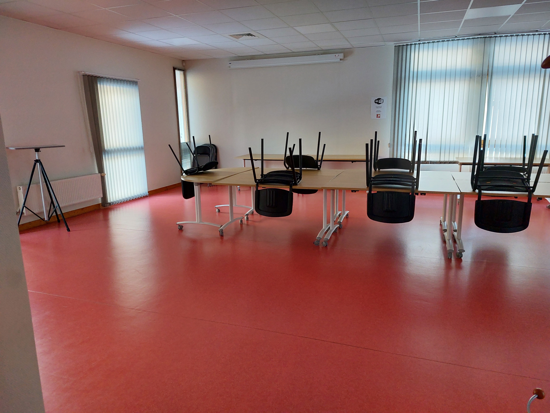 Salle avec tables, chaises, projecteur sur trépied et fenêtres.