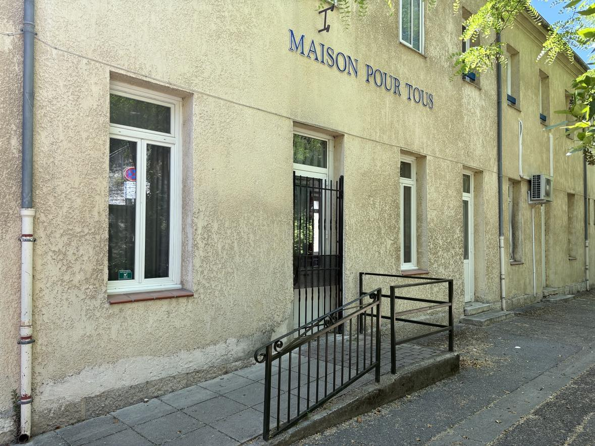 Bâtiment avec enseigne "Maison Pour Tous", porte avec rampe, fenêtres et climatiseurs.