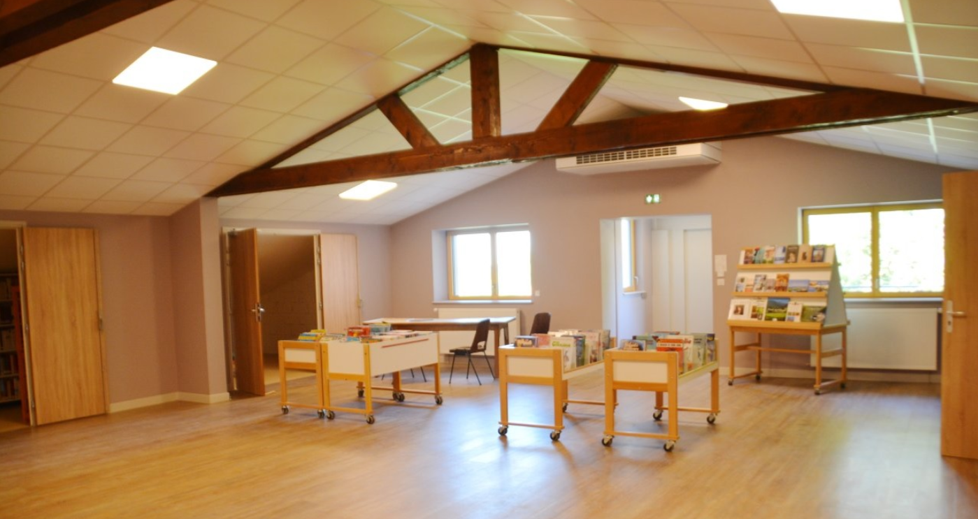 Salle avec tables, chaises, étagères, livres, portes et fenêtres.