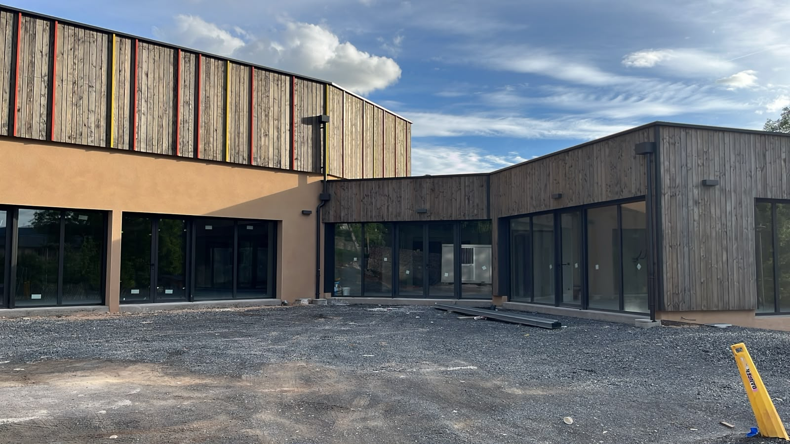 Bâtiment moderne avec façade en bois et verre, parking graviers.