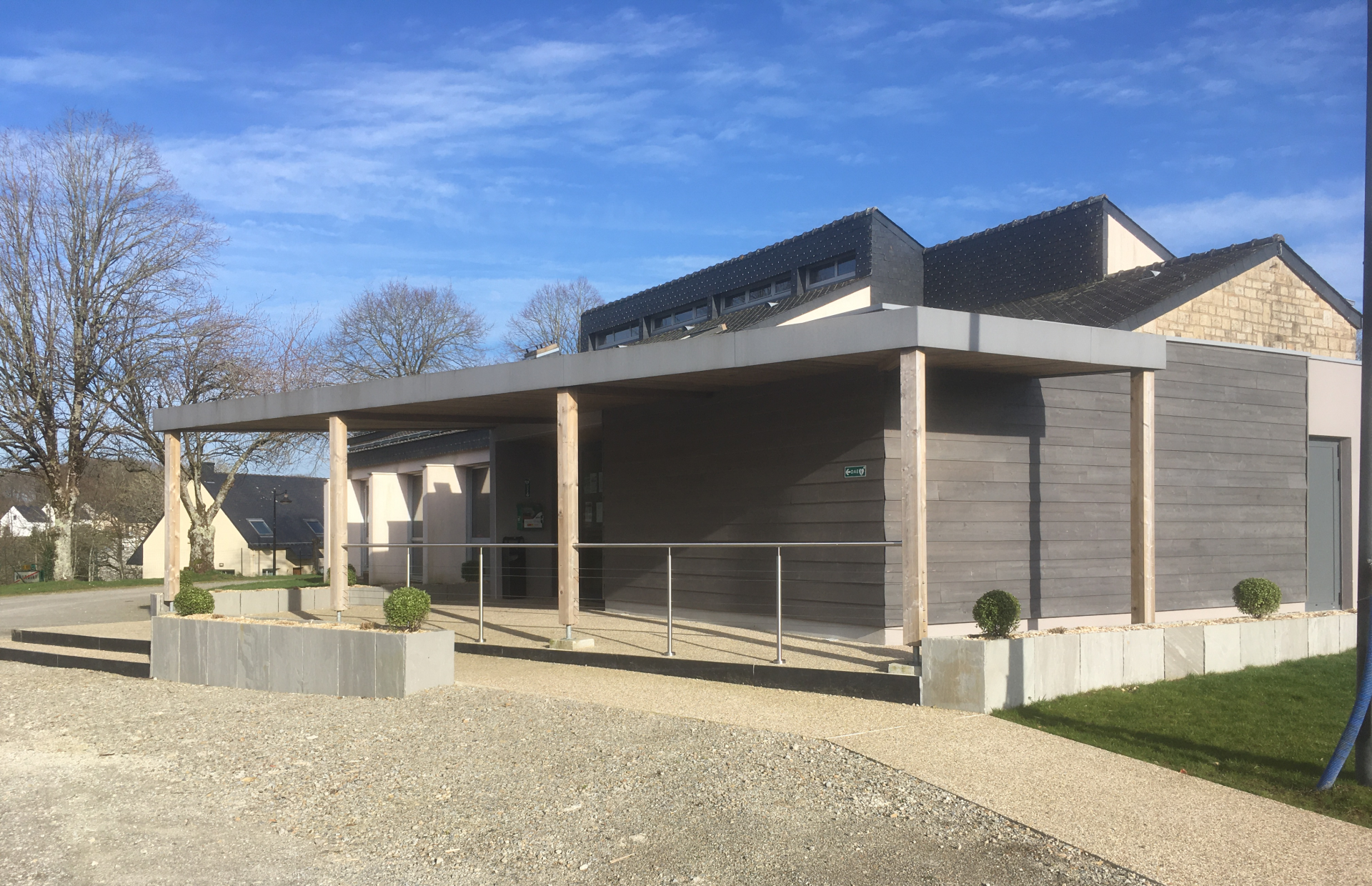 Bâtiment moderne avec colonnes, toit plat, entrées vitrées et allée gravillonnée.