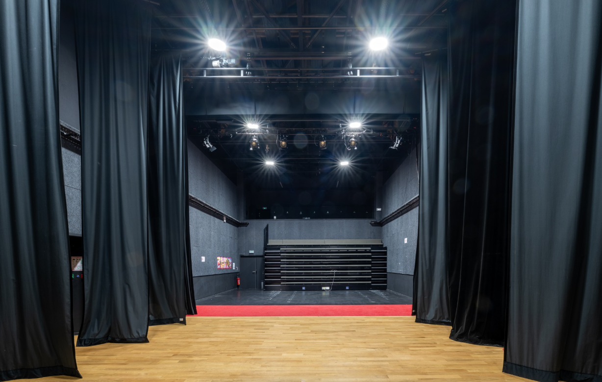Salle de spectacle avec scène, projecteurs, rideaux et gradins.