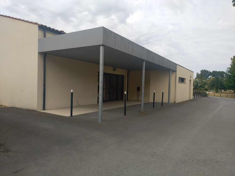 Bâtiment beige avec auvent, portes et poteaux.