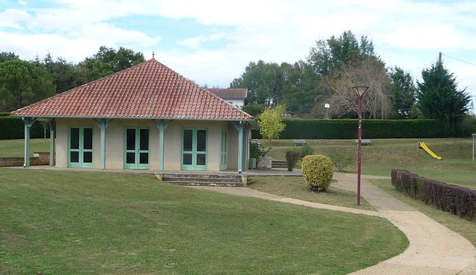 Maison avec toit rouge, fenêtres vertes, gazon, sentier, banc, lampadaire.
