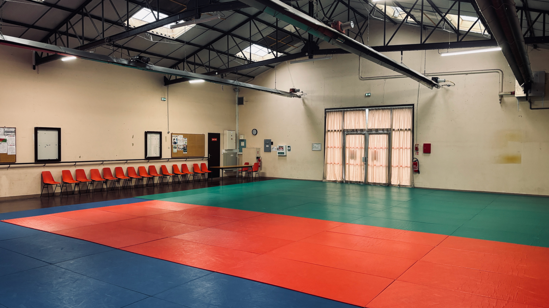 Salle avec tapis de combat, chaises, table et portes.