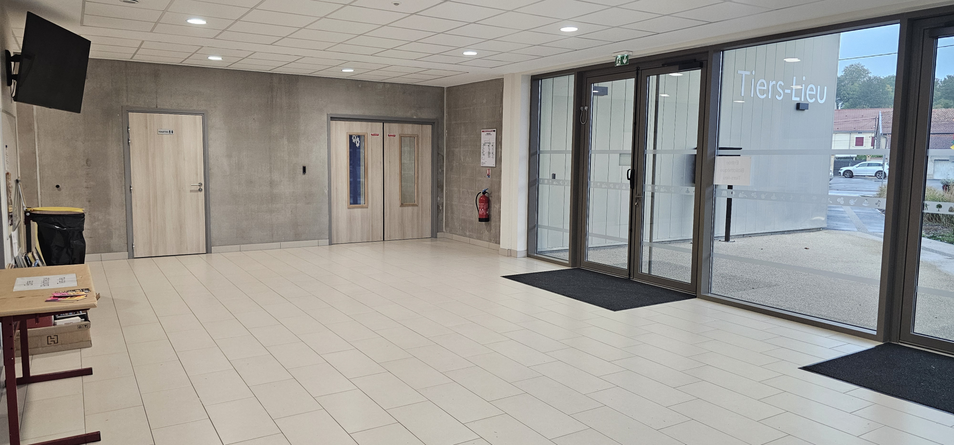Pièce avec portes, écran, table, chaises et extincteur.