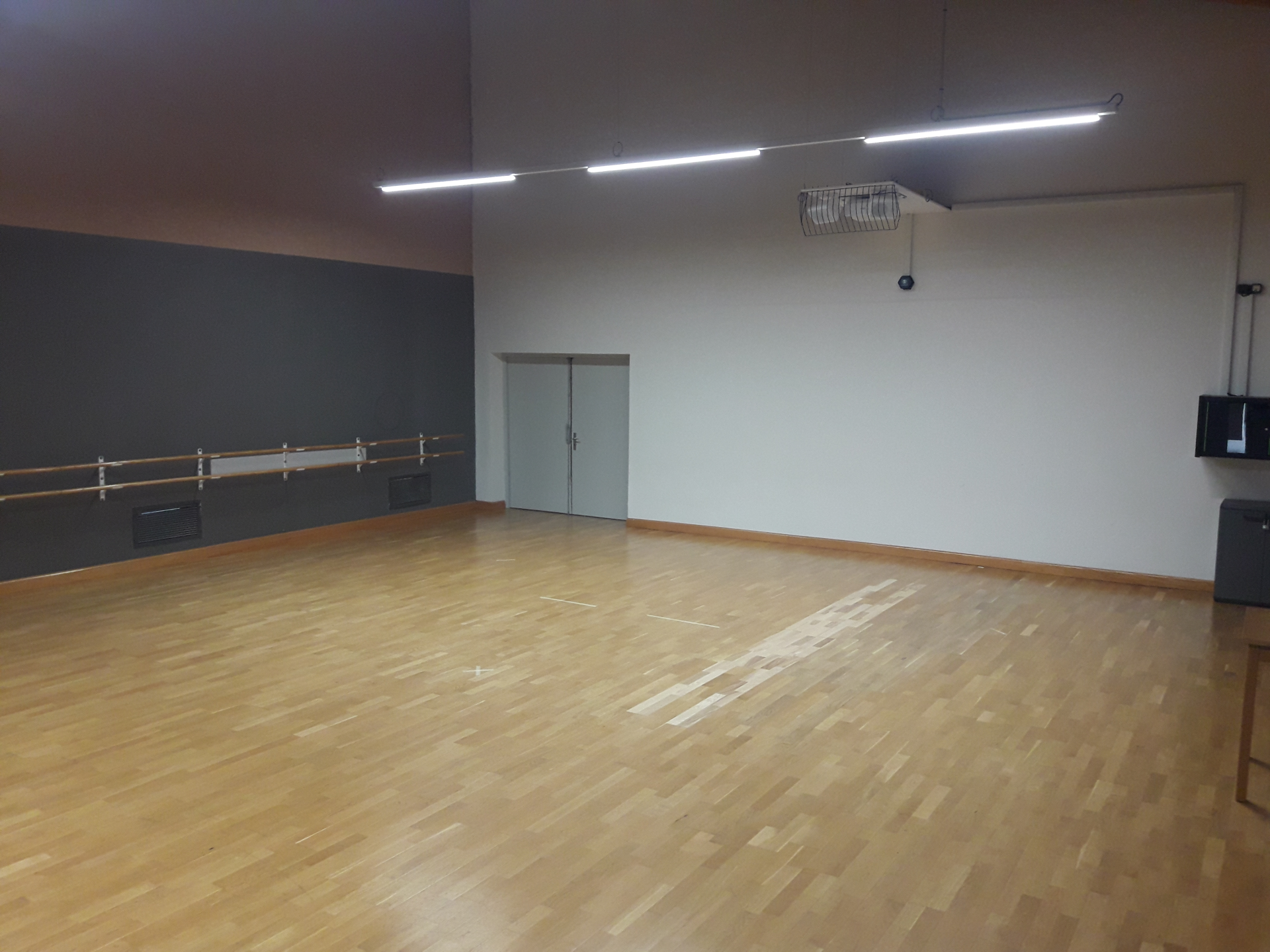 Salle avec parquet, barre de danse, porte, climatiseur et lumières.