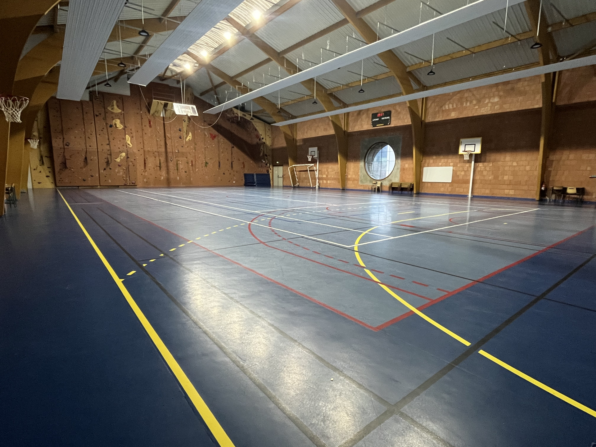 Gymnase avec paniers de basket, paroi d'escalade et lignes de sol.
