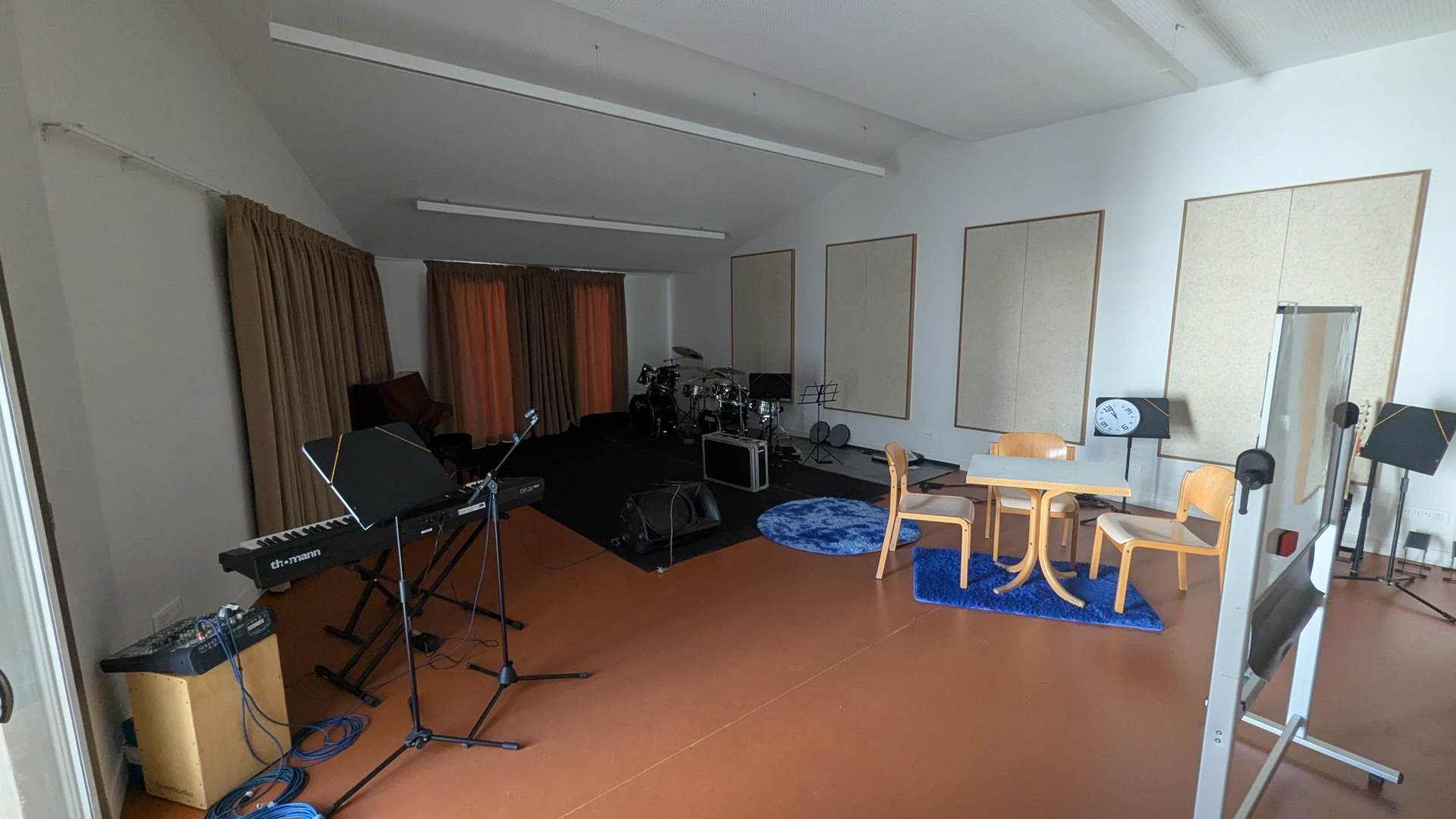 Studio avec clavier, batterie, micros, table, chaises, ampli et matériel audio.