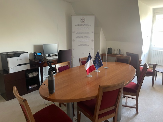 Pièce avec table, chaises, ordinateur, imprimante, et deux drapeaux.