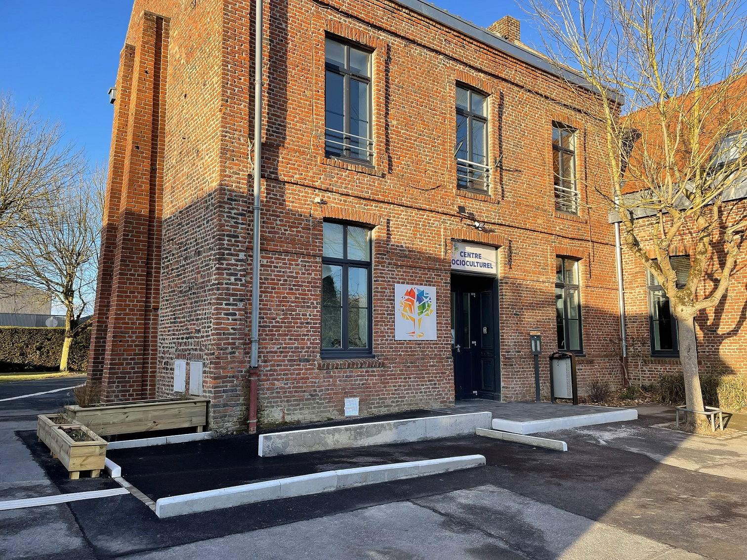 Bâtiment en brique avec entrée, affiche et arbres.