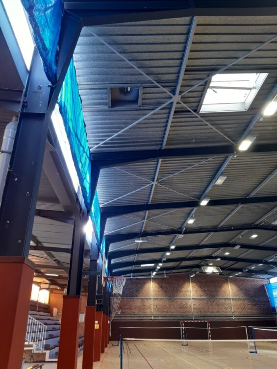 Gymnase avec filets, panneaux de score, gradins, éclairage et toit métallique.