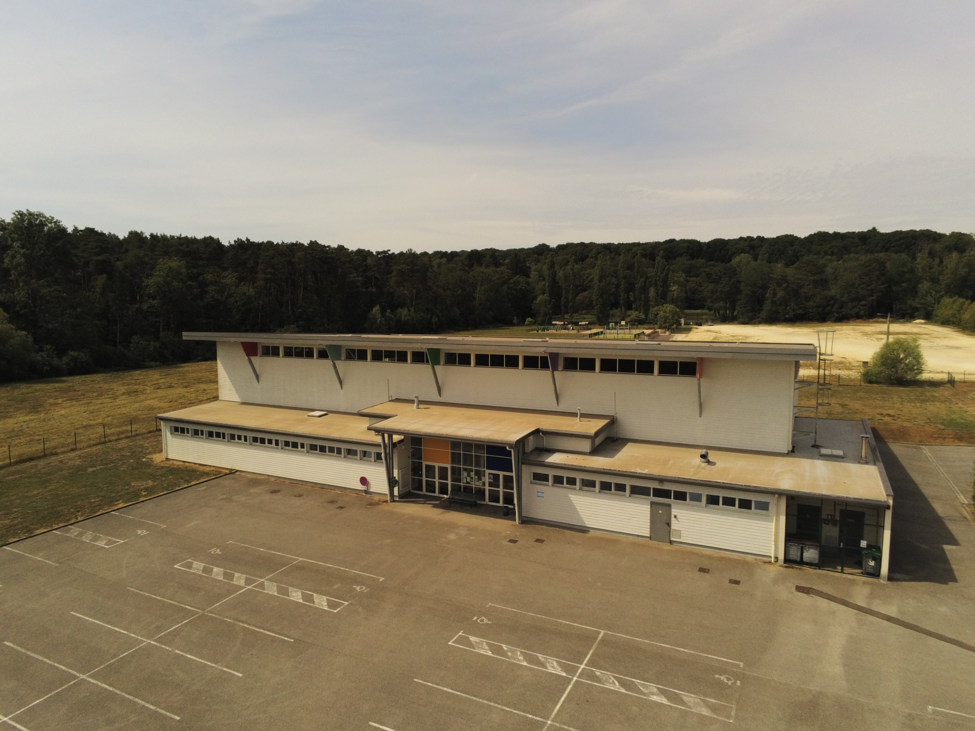 Bâtiment avec parking, forêt en arrière-plan.