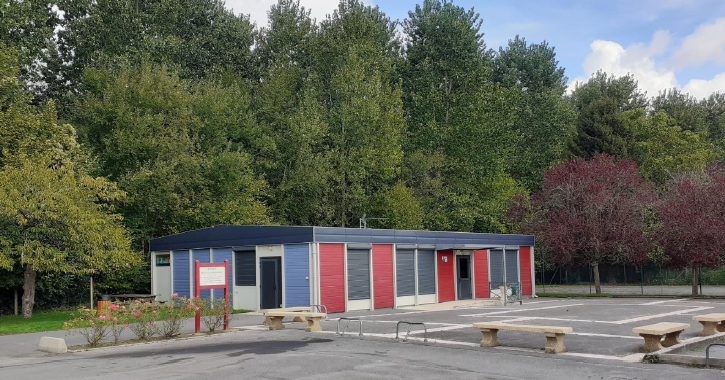 Bâtiment avec portes rouges, tables de pique-nique, et arbres en arrière-plan.