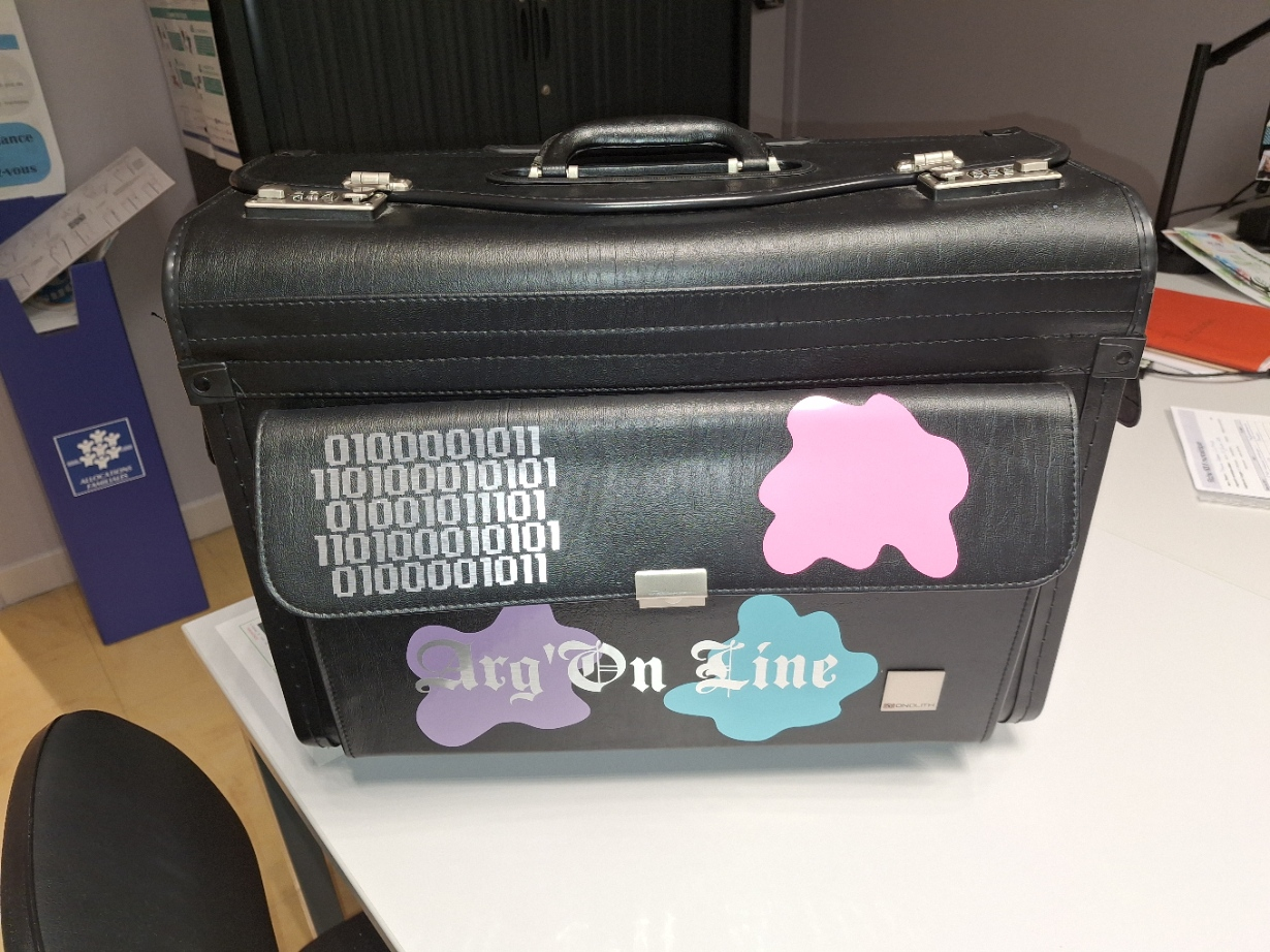 Valise noire avec autocollants et inscriptions, posée sur une table.