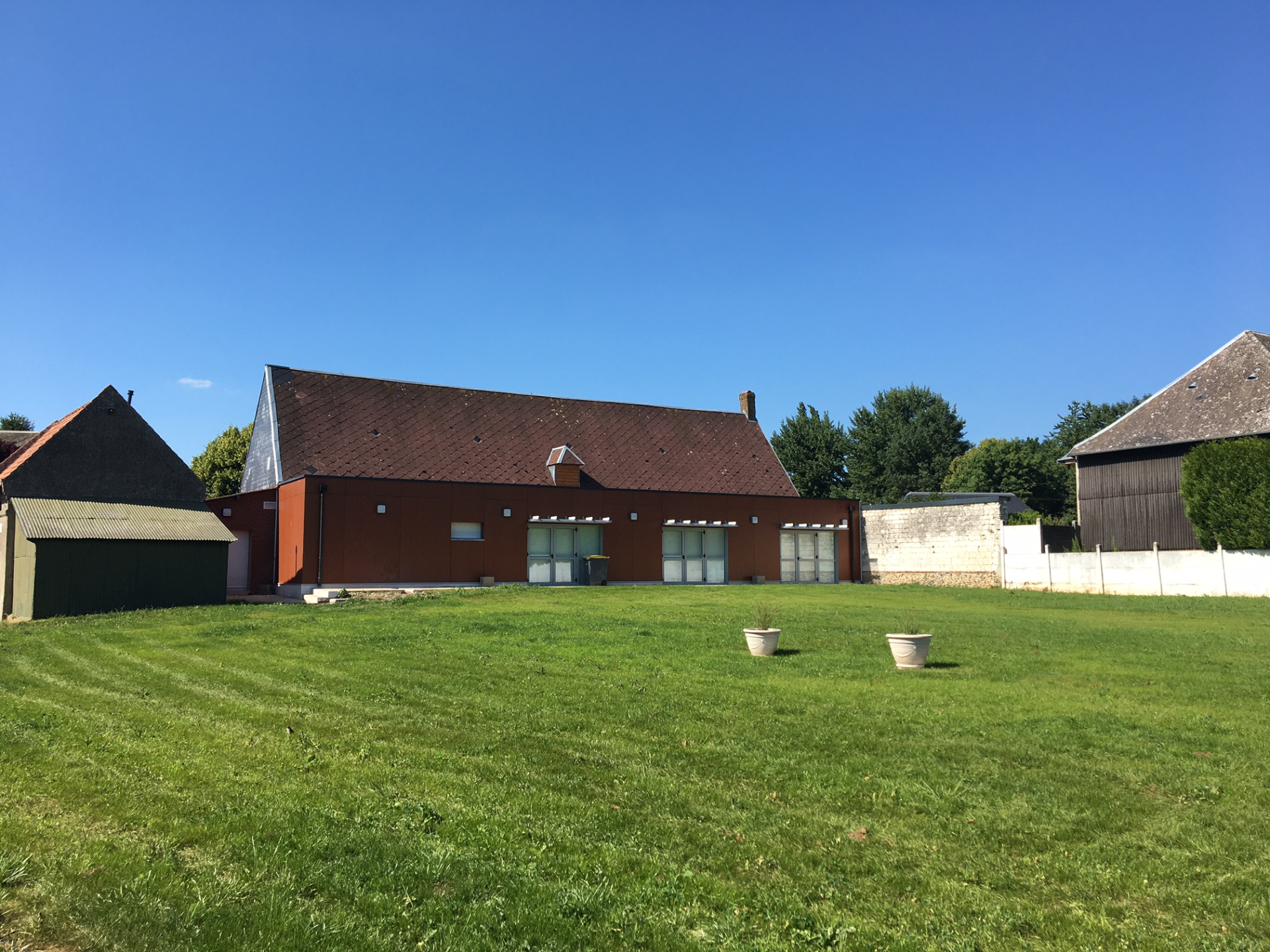 Maison avec toit rouge, trois vasques sur pelouse, ciel bleu.