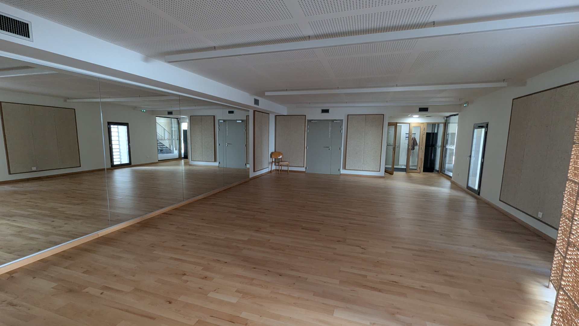 Salle vide avec parquet, miroirs, portes et plafonds suspendus.