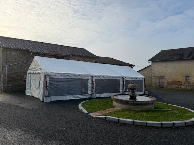 Tente blanche près de bâtiments anciens, fontaine au premier plan.