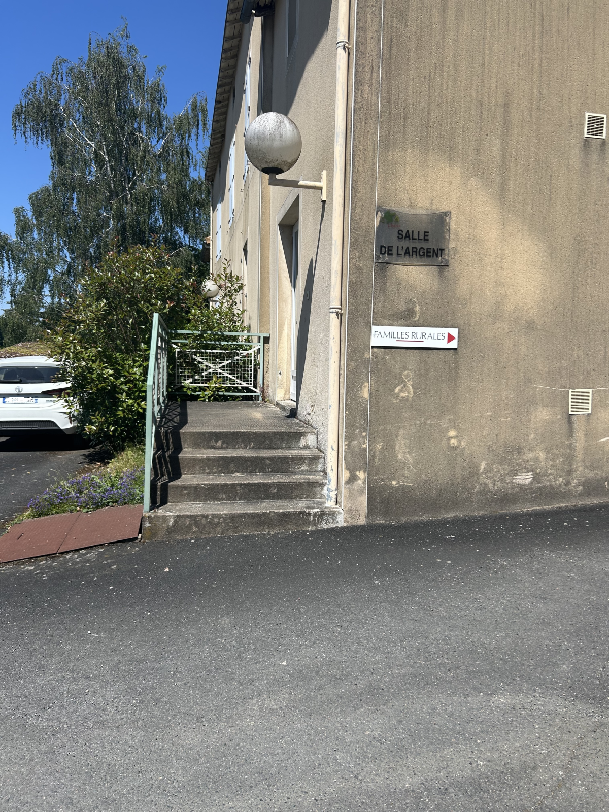 Bâtiment avec escalier, enseigne "Salle de la Mairie", voiture et arbre.