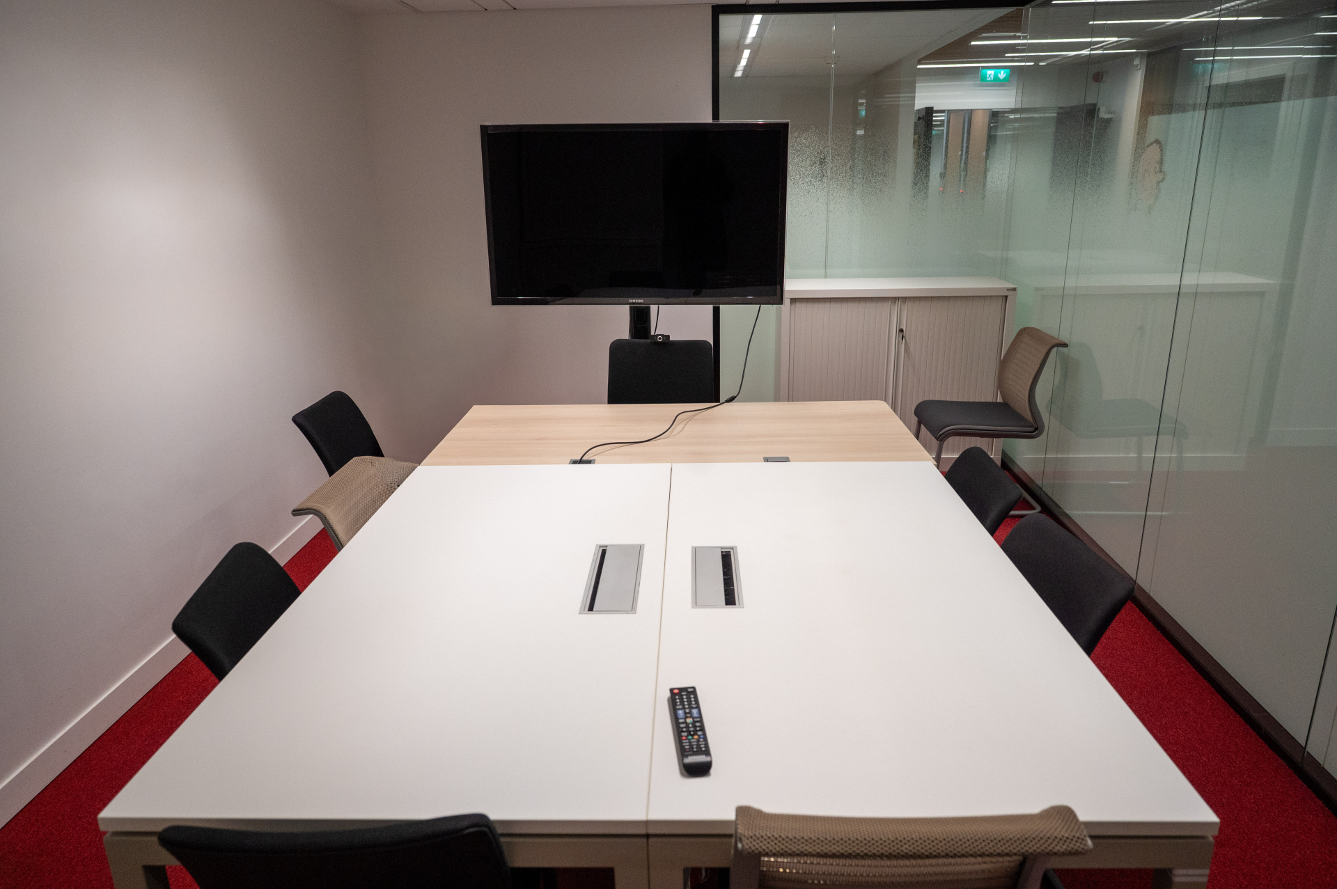 Salle de réunion avec table, chaises, écran, télécommande et armoire.