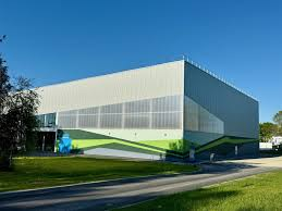 Bâtiment industriel avec façade en verre, peinture verte et bleue, situé près d'une route.