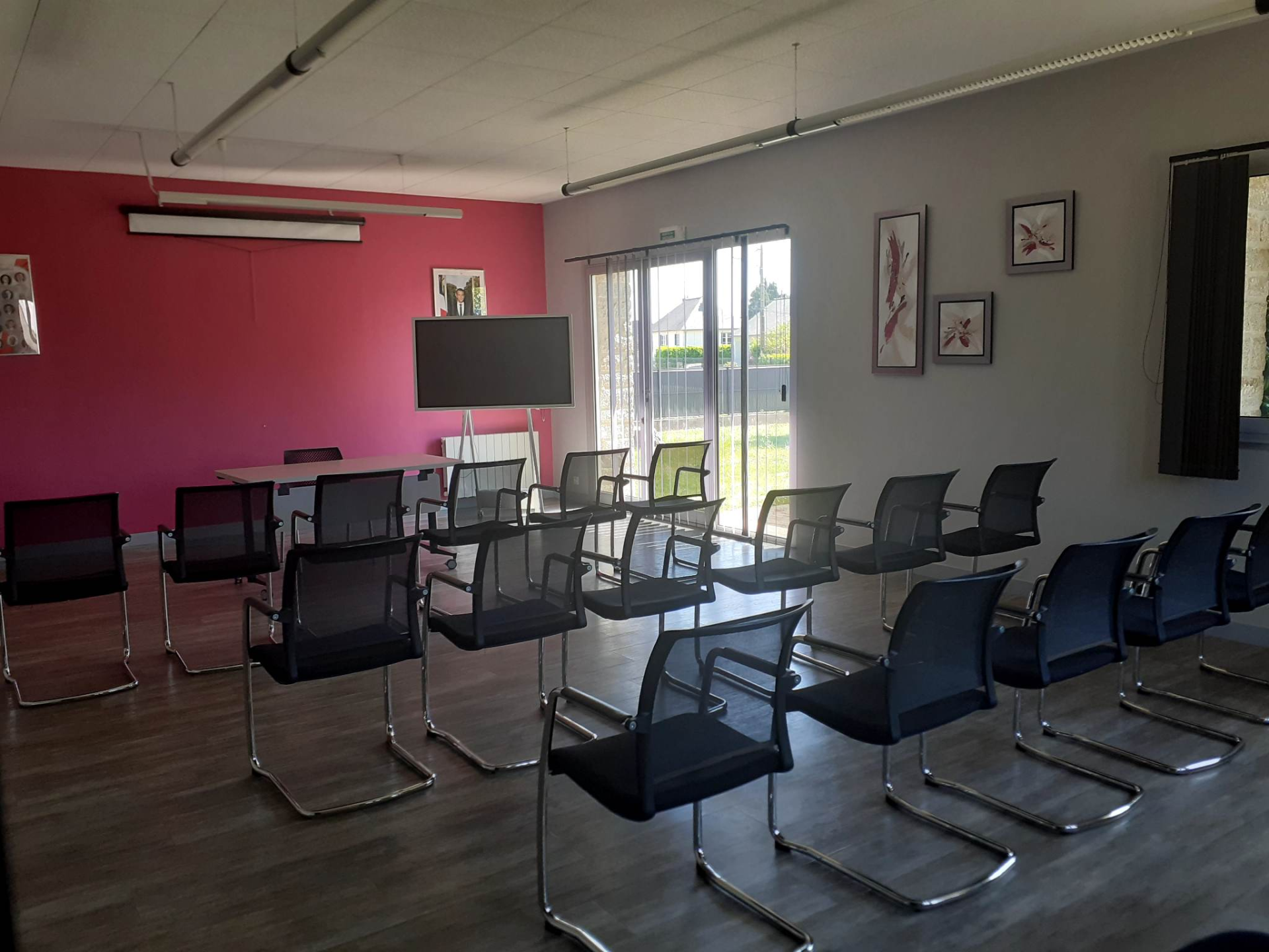 "Salle avec tables, chaises, écran, peintures murales et portes vitrées."