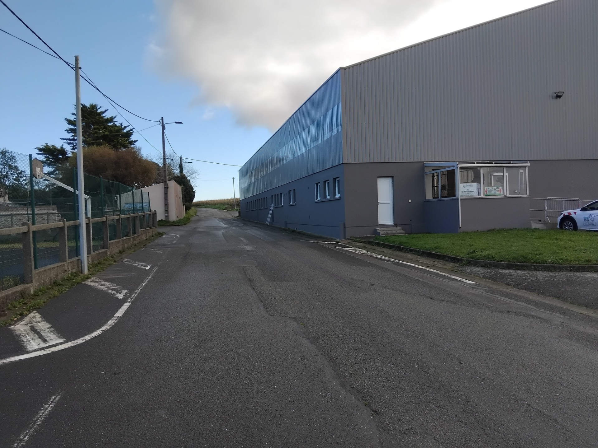 Route menant à un bâtiment industriel avec clôture, lampadaire et voiture.
