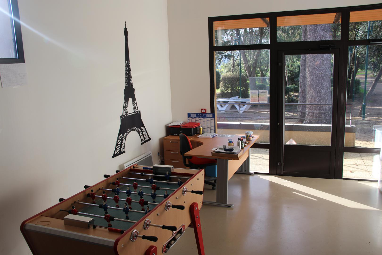 Pièce avec table de football, bureau, chaise, étagères et porte vitrée.
