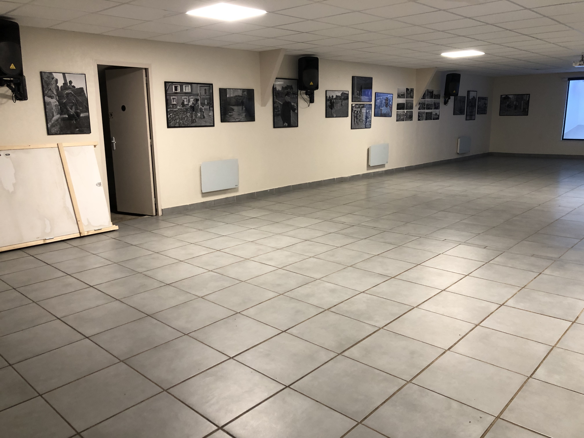 Salle vide avec photos, porte, radiateurs et écran.